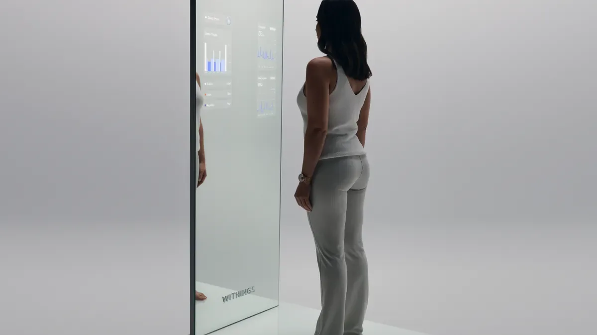 Woman standing in front of a Withings smart mirror that displays health data charts